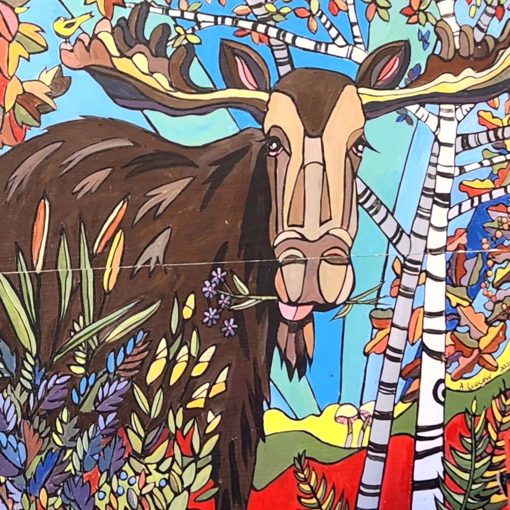 A colorful mural depicting a moose with large antlers, surrounded by vibrant foliage, flowers, and birch trees against a blue sky.