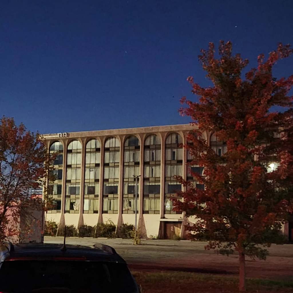 Abandoned building at night with a clear sky and autumn foliage in the foreground.