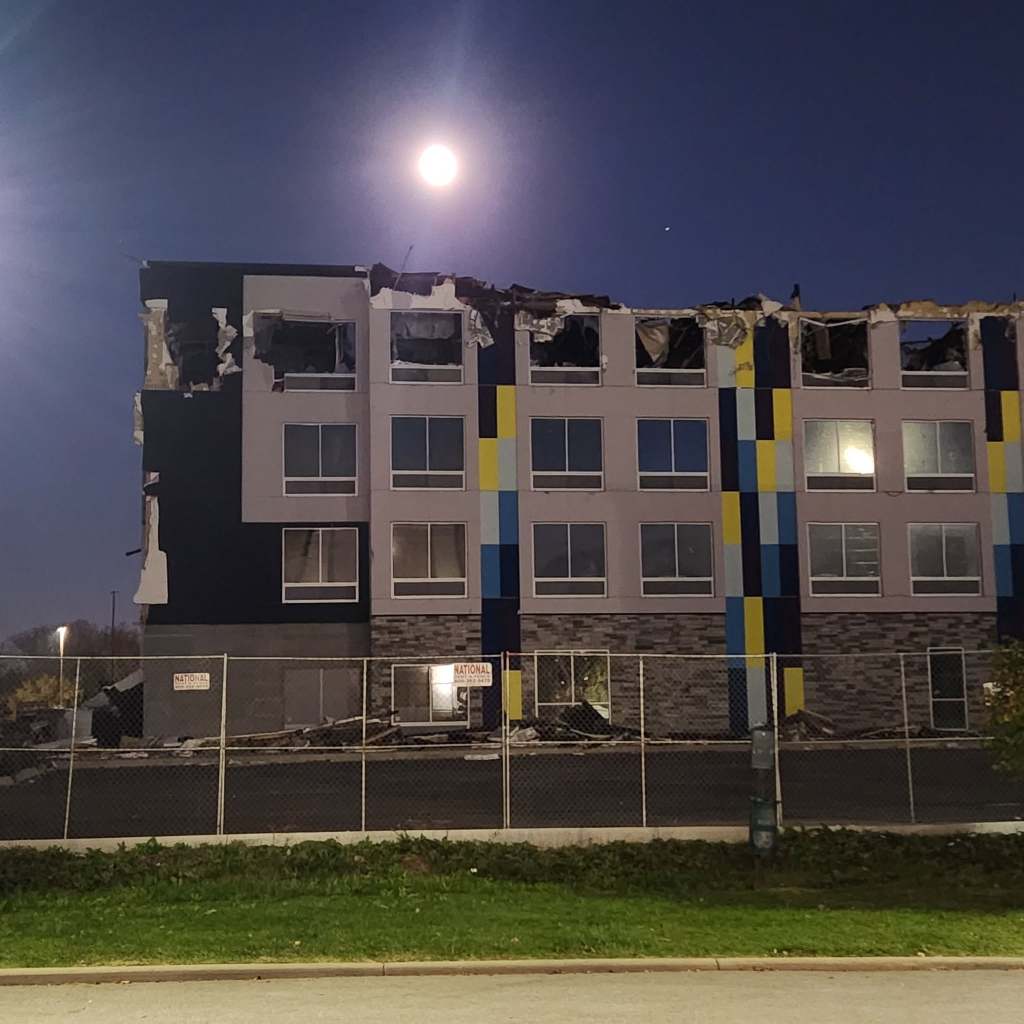 A partially demolished building with missing sections, illuminated by a full moon in the night sky.